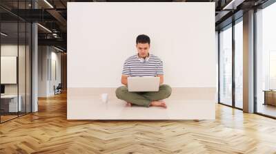 Casual asian man sitting on floor using laptop at home in the living room Wall mural