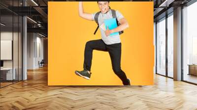 Excited young Asian man jumping with a backpack on the an orange background Wall mural