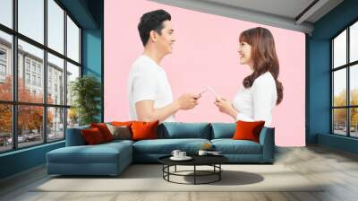 Face-to-face conversation. Excited man and woman talking holding smartphones looking at each other standing over pink Background. Wall mural