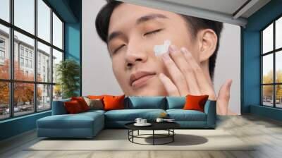 grooming, skin care and people concept - smiling young indian man applying cream to face over white background Wall mural