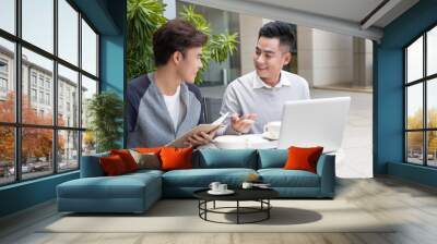 Handsome Asian business colleagues or college students work together using laptop, startup project meeting or teamwork brainstorm concept, at coffee shop or modern office Wall mural