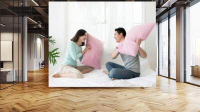 Happy asian couple having pillow fight in bed at home. Family fu Wall mural