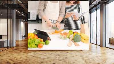 Happy couple in kitchen together. Man cutting vegetables and making salad while his wife reading recipe Wall mural