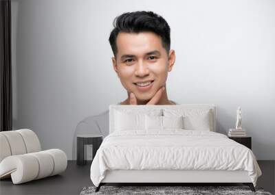 Happy smiling young handsome Asian man face with hand touching chin studio shot isolated Wall mural