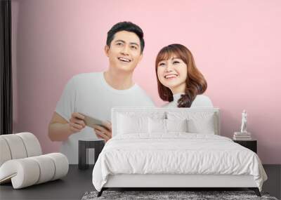 Image of excited couple man and woman smiling while both using mobile phones isolated over pink background Wall mural