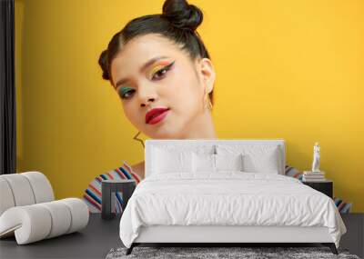 Nice-look girl with buns cute smiles. Woman with colorful eye-shadows poses on yellow background Wall mural