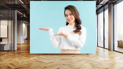 Portrait of Asian beautiful young girl raising both hands aside show something, isolated in blue background. Wall mural