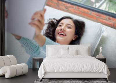 Portrait of young smiling woman lounging in bed and writing to diary in home interior Wall mural