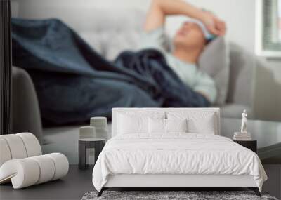 sick wasted man lying in sofa suffering cold and winter flu virus having medicine tablets in health care concept looking temperature on thermometer Wall mural