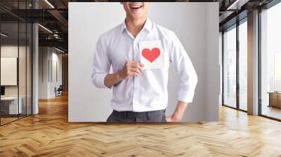 Smiling man holding valentine's card standing on a white background Wall mural