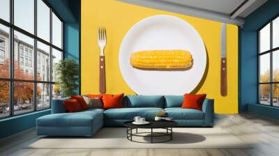 Top view of corn on white plate with knife and fork on yellow background Wall mural