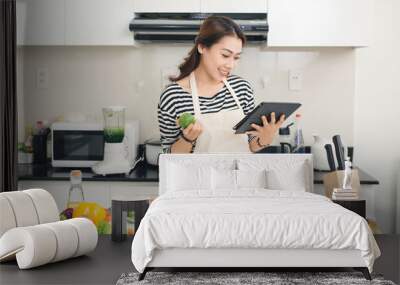 Young asian woman using a tablet computer to cook in her kitchen Wall mural