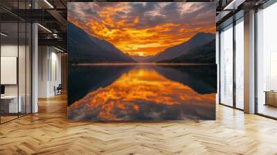 Fiery sunrise emerging from behind distant mountains, casting golden hues across the sky and reflecting over a tranquil lake. Wall mural