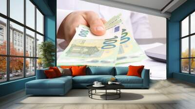 a man's hand holds out one hundred euro bills against the background of an office table with a computer Wall mural