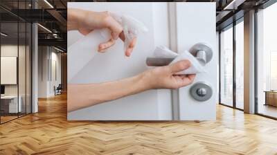 Cleaning white door handles with an antiseptic wet wipe and sanitizer spray. Disinfection in hospital and public spaces against corona virus. Woman hand using towel for cleaning home room door link. Wall mural