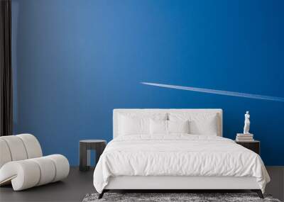 Flying passenger plane on a blue sky with a white smoke trail. Photos of aviation from the ground. Cargo transportation by airplane, air travel. On a sunny clear day. Wall mural