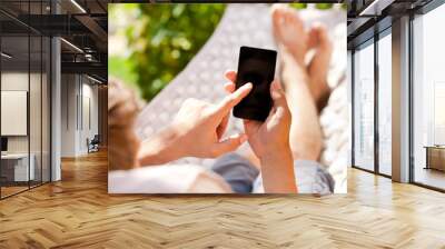 man using mobile smart phone while relaxing in a hammock Wall mural