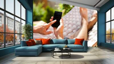 Man using mobile smart phone while relaxing in a hammock Wall mural