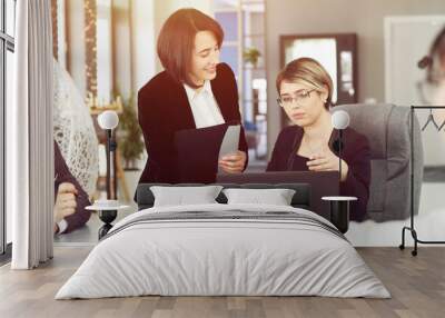 Two young business women in the office, analyzing information looking into a laptop and smiling Wall mural