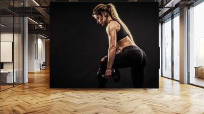 Fitness in gym, sport and healthy lifestyle concept. Beautiful athletic woman showing her trained body on black background. Bodybuilder female model training triceps muscles with dumbbell. Wall mural