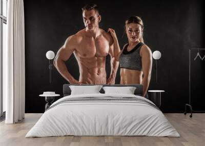 Fitness in gym, sport and healthy lifestyle concept. Couple of athletic man and woman showing their trained bodies on black background. Two bodybuilder models standing and demonstrating tight muscles. Wall mural