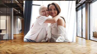 Mother and daughter relationship concept. A woman congratulates happy teenage girl on her birthday and gives her warm hugs. The family celebrates anniversary at home. Wall mural