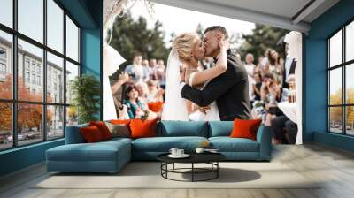 A bride and a groom are kissing in front of the guests. Wall mural