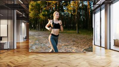 Smiling girl running in the wood, listening to music in headphones, . Dressed in sportswear. Lifestyle, sport concept. Wall mural