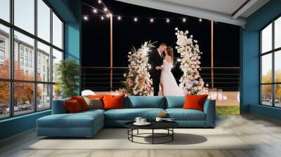 The bride and groom near the arch at the evening ceremony. Wall mural