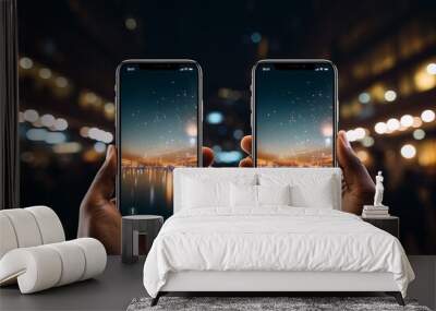 Two hands holding smartphones displaying a night cityscape by a reflective body of water Wall mural