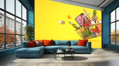 Shopping basket full of grocery products, food and drink on yellow background. Wall mural