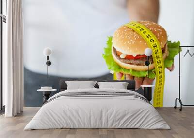 Diet concept, woman holding harmful fat burger with yellow measuring tape. Wall mural