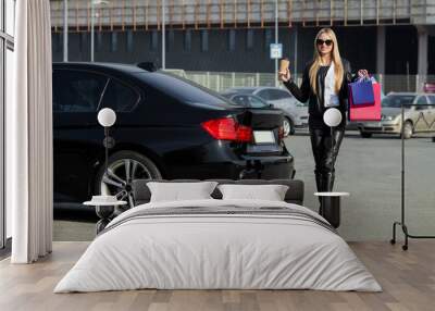 Woman holding colored bags near her car in black friday holiday Wall mural