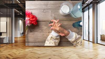 child washes and disinfects hands with an antiseptic on a wooden background. hands in the frame. on the table are liquid soap in the dispenser. Wall mural