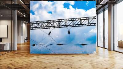 Iron mast with high voltage electric power wires of the railway. Railway. Transport infrastructure. Electric wires for powering trains. Industrial equipment. Blue sky with clouds. Wall mural