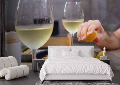 A hand squeezing a lemon over a plate of fried squids with two glasses of white wine Wall mural