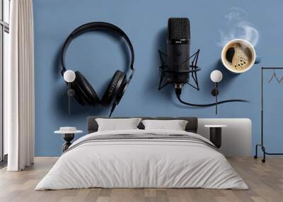 A flat lay, top-down view of a music or podcast setup on a blue table. Black headphones rest next to a sleek recording microphone, a steaming cup of coffee, and an open laptop. Wall mural