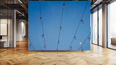 Low angle view of light bulb garland, decorative lights, against blue sky with full moon at dusk. Wall mural