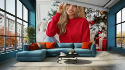 Close-up of a young woman sitting on the back of a sofa with the Christmas tree in the background Wall mural