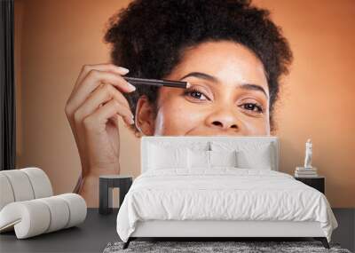 Eyeliner, beauty and portrait of a black woman doing a cosmetic makeup routine in the studio. Cosmetics, beautiful and happy African model doing eye make up with pencil isolated by orange background. Wall mural