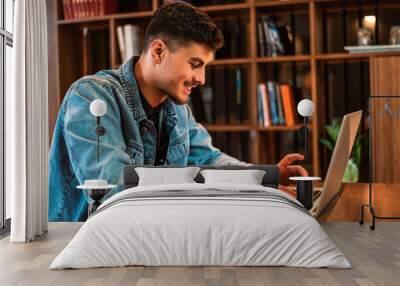 A happy male college student using a laptop in a university library. Wall mural