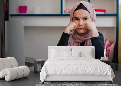 A sad and bored Muslim student girl while learning for school at home desk. Wall mural