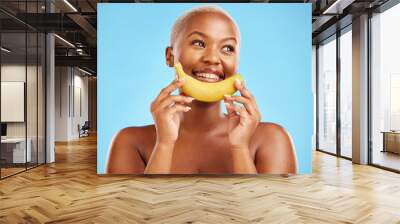 Beauty, smile and banana with a model black woman thinking on a blue background in studio. Skincare, idea and food with a happy young female person holding yellow fruit for natural wellness or detox Wall mural