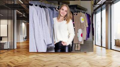 Beautiful young woman in a luxurious white sweater posing in mall on the background of clothes and hangers Wall mural