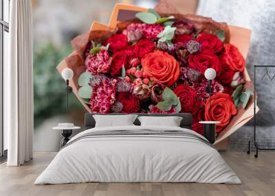 beautiful fresh cut bouquet of mixed flowers in woman hand. the work of the florist at a flower shop. Bright juicy red colors Wall mural