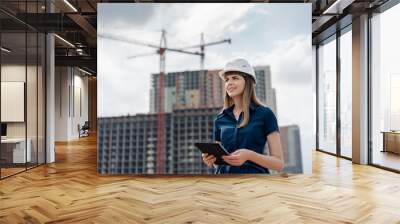 Female construction engineer. Architect with a tablet computer at a construction site. Young Woman looking, building site place on background. Construction concept Wall mural