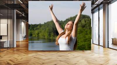 Happy woman standing with arms raised, saluting the sun outdoors Wall mural