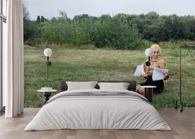 Woman is sitting in a field with a laptop open in front of her Wall mural