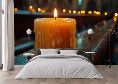 A single candle burns brightly on a wooden pew in a dimly lit church, surrounded by other candles. Wall mural