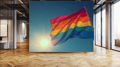 Rainbow Pride flag waving in the wind against a blue sky with the sun shining. Wall mural